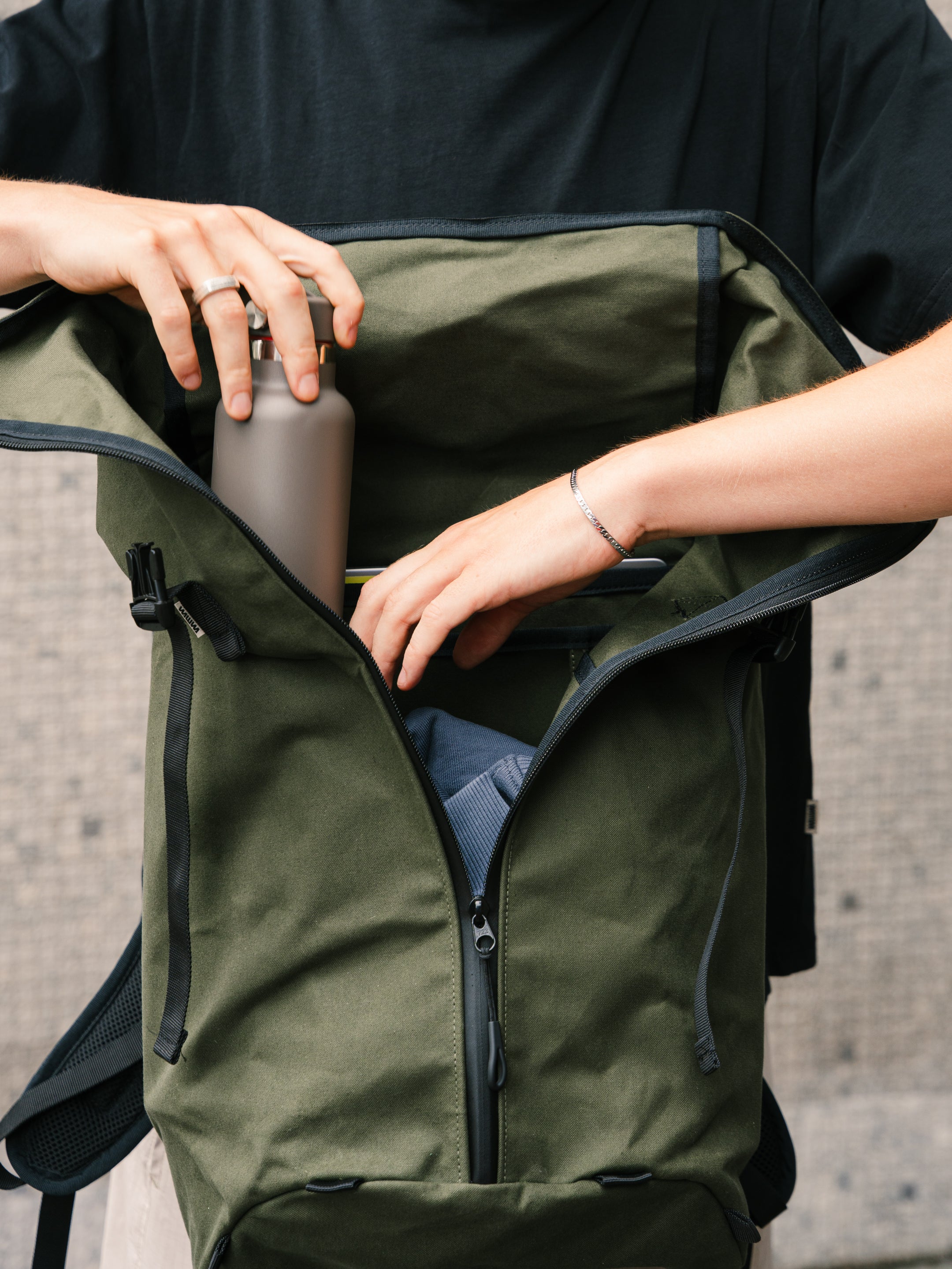 Bridge Backpack in Khaki Green with roll-top open, water bottle being packed inside