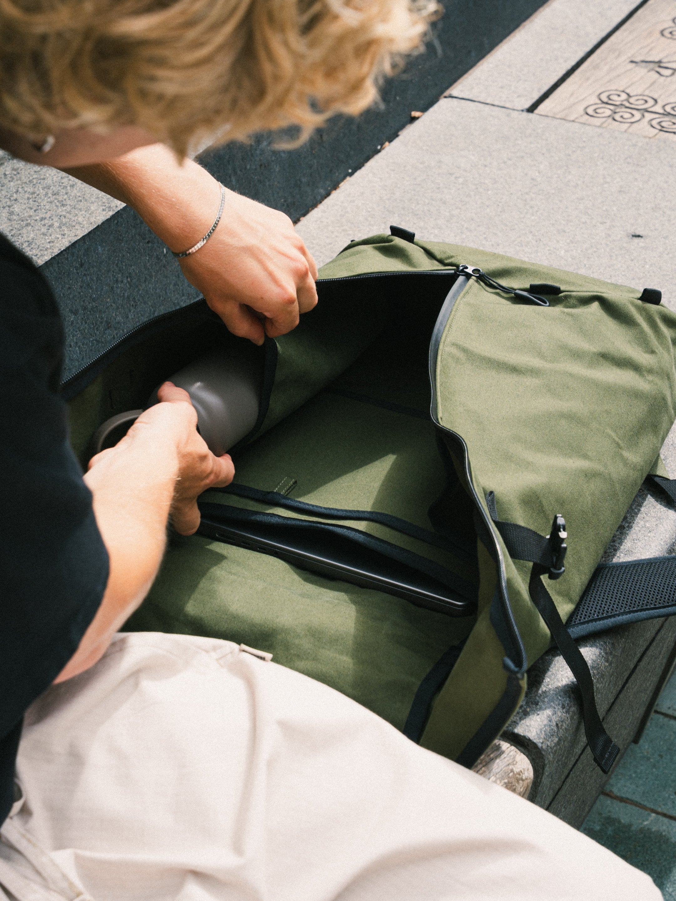 Packing a bottle into the Bridge Backpack in Khaki Green on a city street